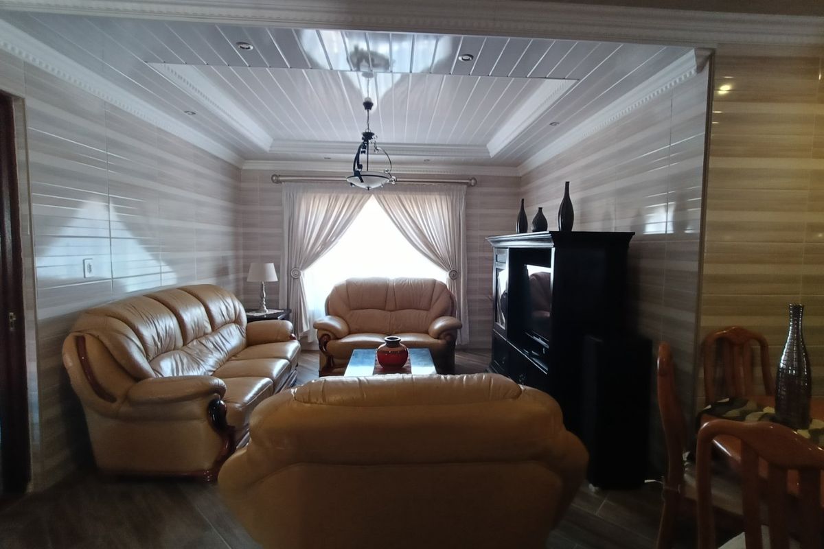 A living room featuring tiled wall finishes, wood-look floor tiles, and a coved ceiling with recessed lighting.