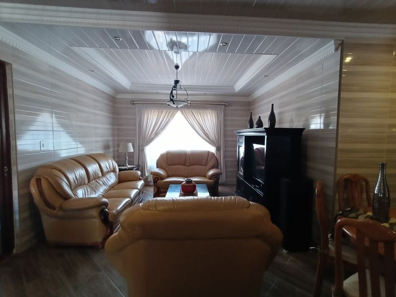 A living room featuring tiled wall finishes, wood-look floor tiles, and a coved ceiling with recessed lighting.