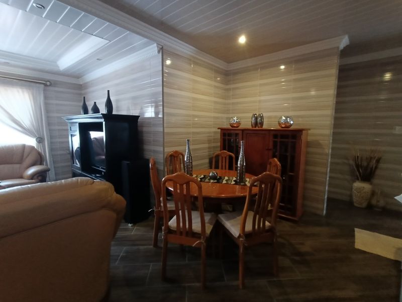 A living and dining area featuring tiled wall finishes, dark floor tiles, and a coved ceiling with recessed lighting.