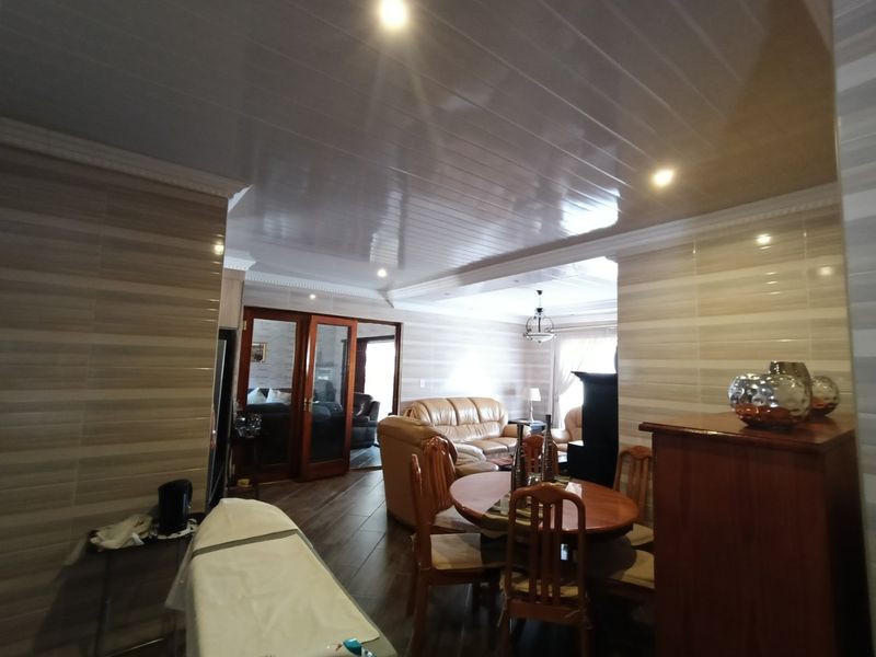 Open plan living and dining area featuring tiled walls, glossy ceiling panels, and timber framed glass doors leading to an adjacent room.