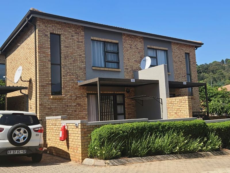 Front elevation of a double-storey face brick townhouse featuring a paved driveway, carport, and neat landscaped garden border.