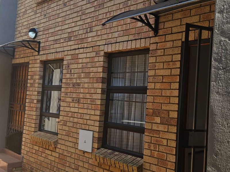 Front facade of a townhouse featuring face brick construction, security gates, and protective window awnings over the entrance and window areas.