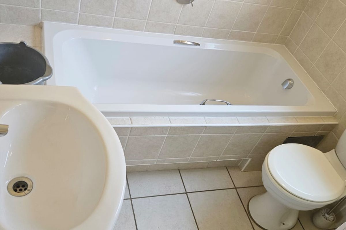 A functional bathroom featuring a built-in bathtub, pedestal washbasin, and dual-flush toilet with neutral ceramic tiling throughout.