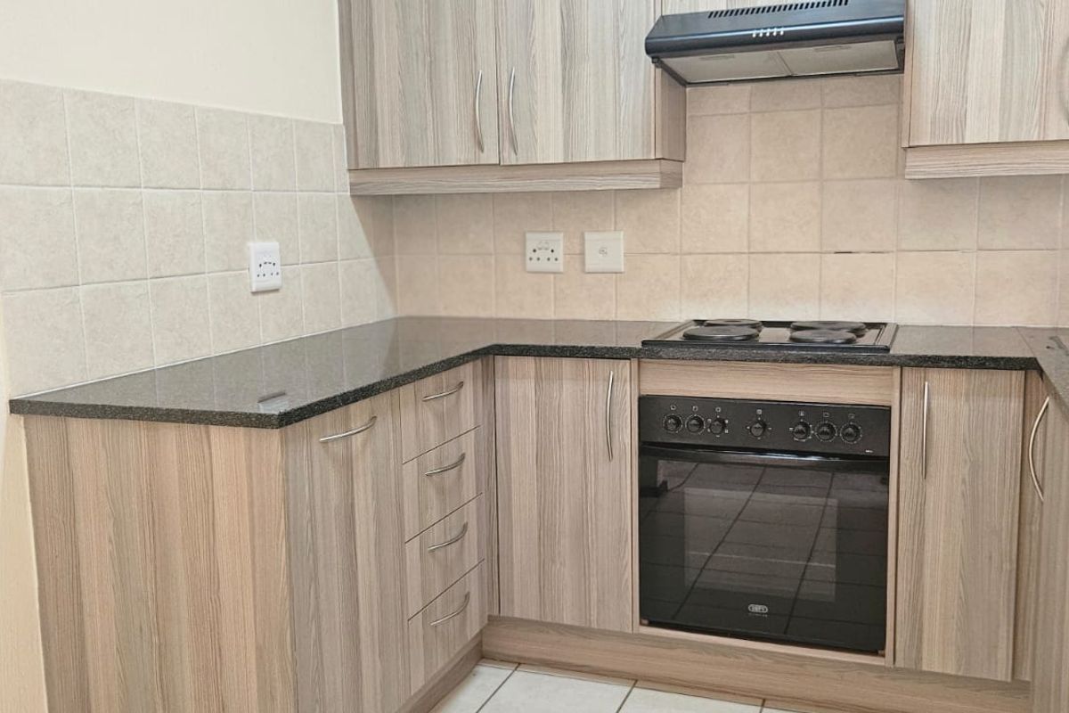 A functional kitchen featuring wood-look cabinetry, granite countertops, a built-in oven with electric hob, and a tiled backsplash.