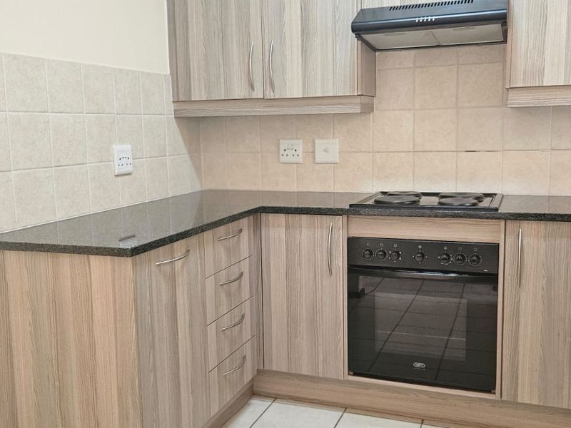 A functional kitchen featuring wood-look cabinetry, granite countertops, a built-in oven with electric hob, and a tiled backsplash.
