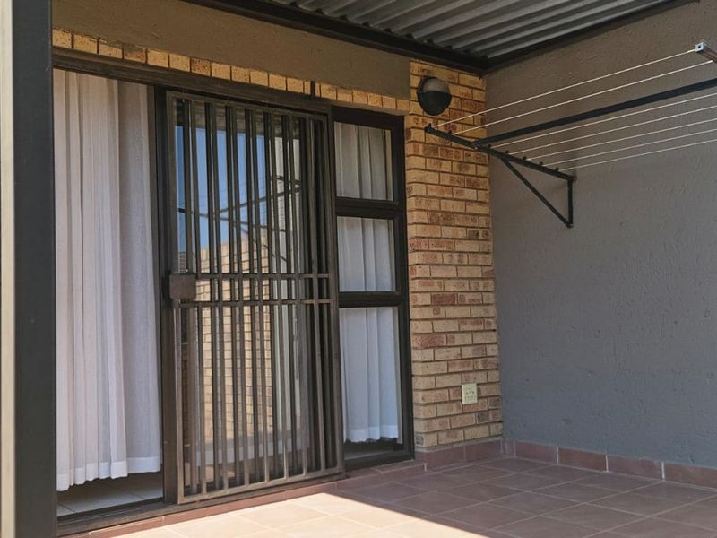 A covered patio area featuring tiled flooring, brick wall accents, and a secure sliding door entrance with an integrated wall-mounted drying rack.