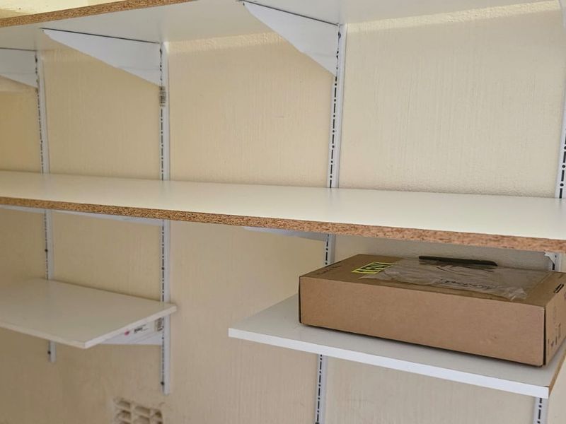 A utility storage area featuring functional wall-mounted adjustable shelving units with white laminate finish.