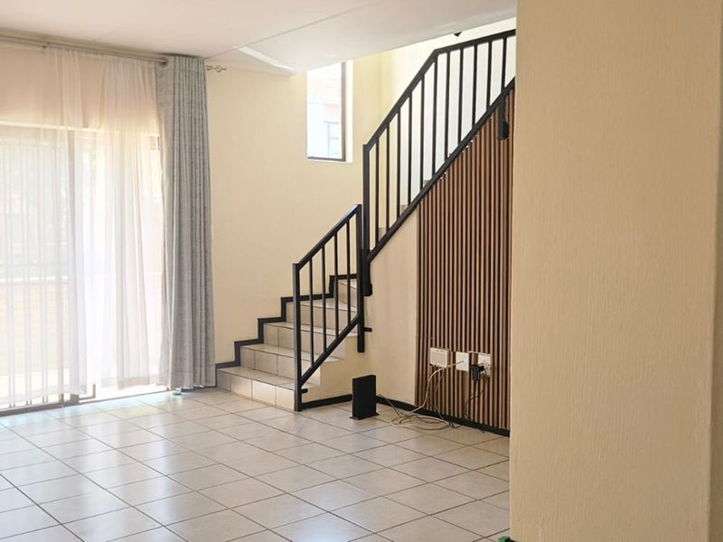 Open-plan living area featuring tiled floors, a modern staircase with a slatted wood feature wall, and an adjacent kitchen with built-in cabinetry.