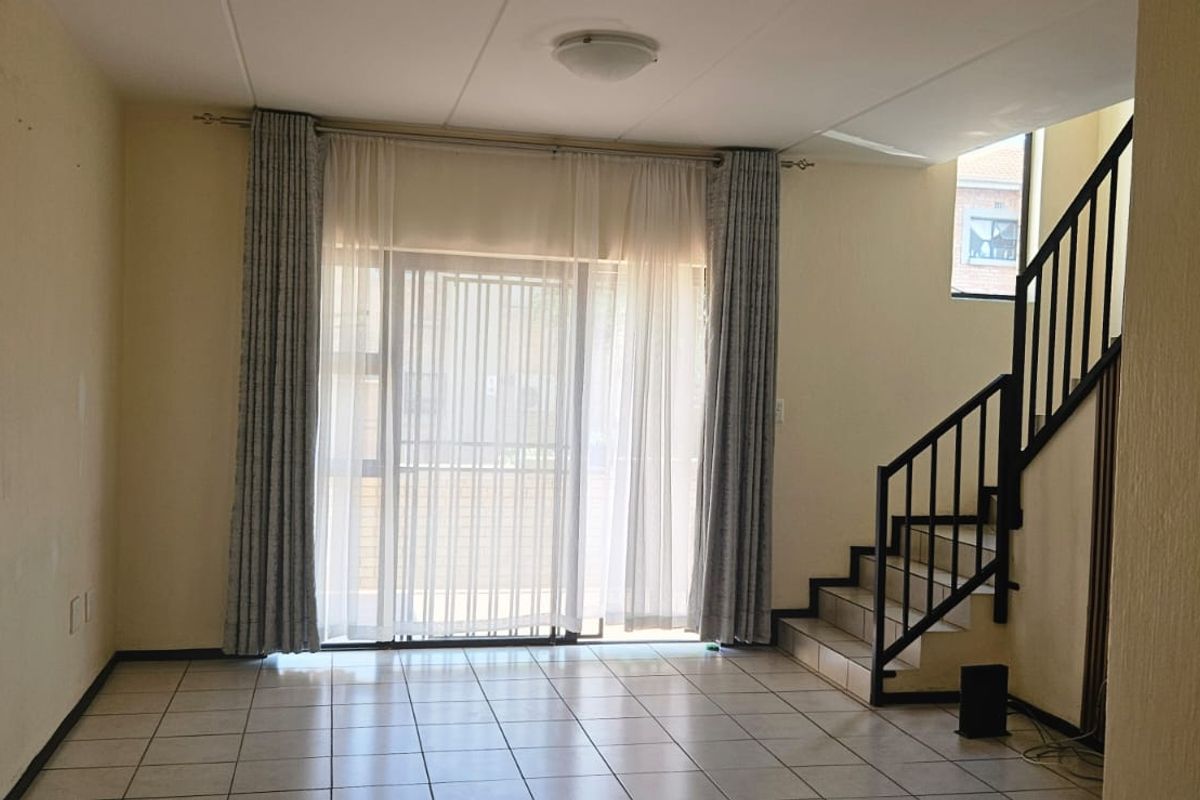 An empty living room featuring tiled flooring, a staircase with a metal railing, and a sliding glass door leading to the exterior.