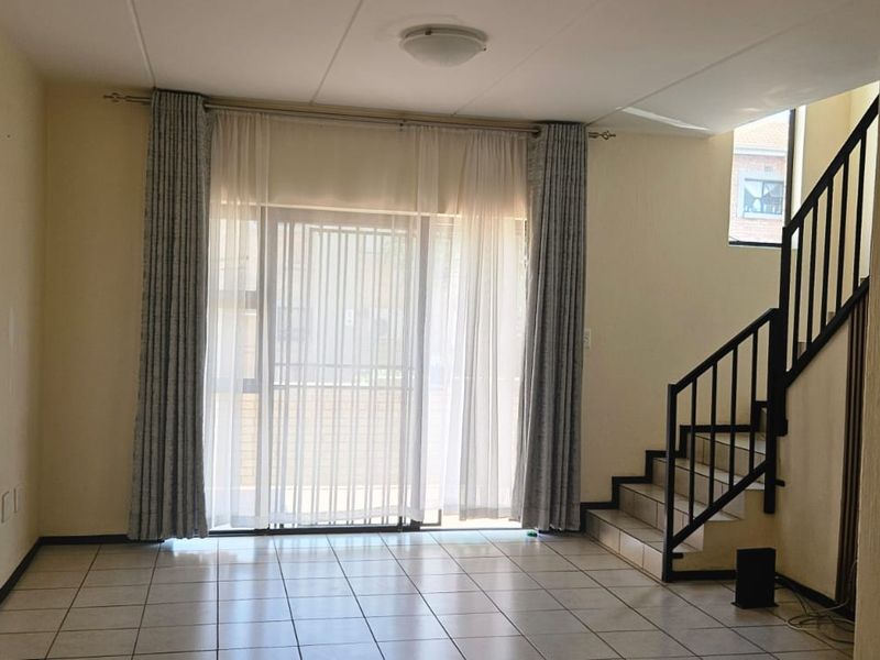 An empty living room featuring tiled flooring, a staircase with a metal railing, and a sliding glass door leading to the exterior.