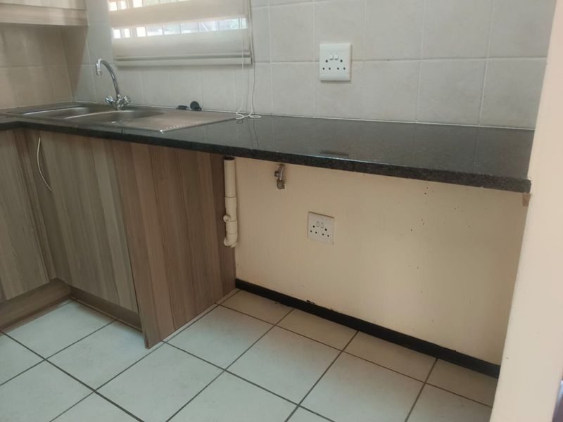 A functional kitchen area featuring granite countertops, a stainless steel sink, tiled backsplash, and dedicated plumbing and electrical points for appliances.
