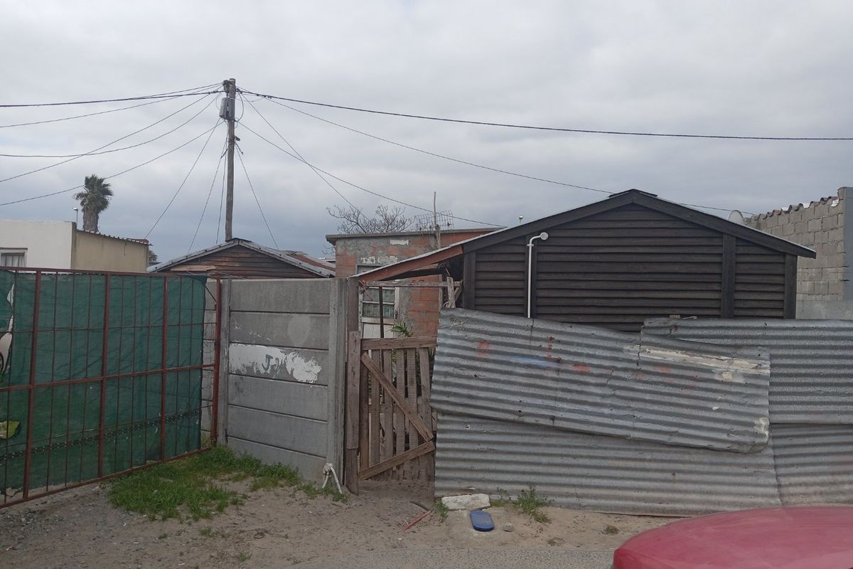 Rear exterior view showing basic boundary fencing, timber structures, and utility connections in a weathered condition.