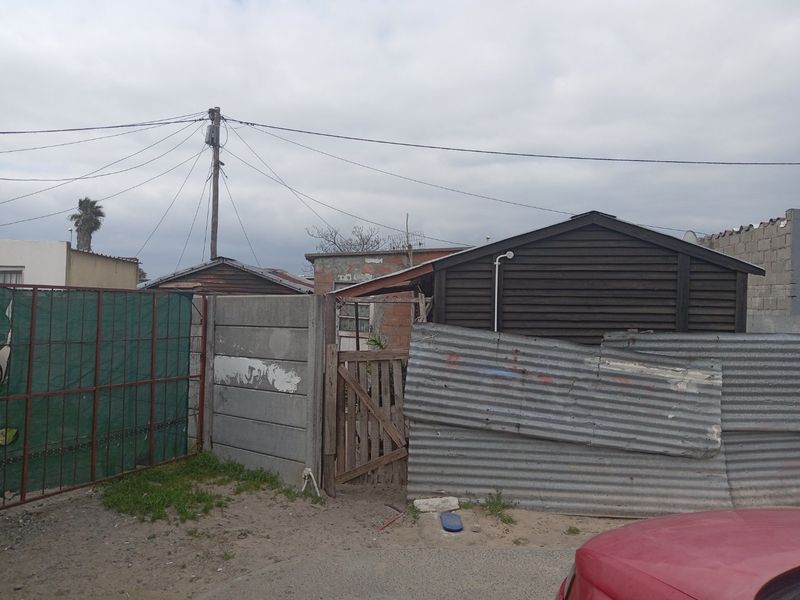 Rear exterior view showing basic boundary fencing, timber structures, and utility connections in a weathered condition.