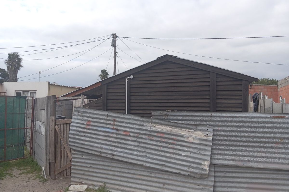 Rear view of the property featuring timber-clad structure, corrugated metal fencing, and precast concrete boundary walls.