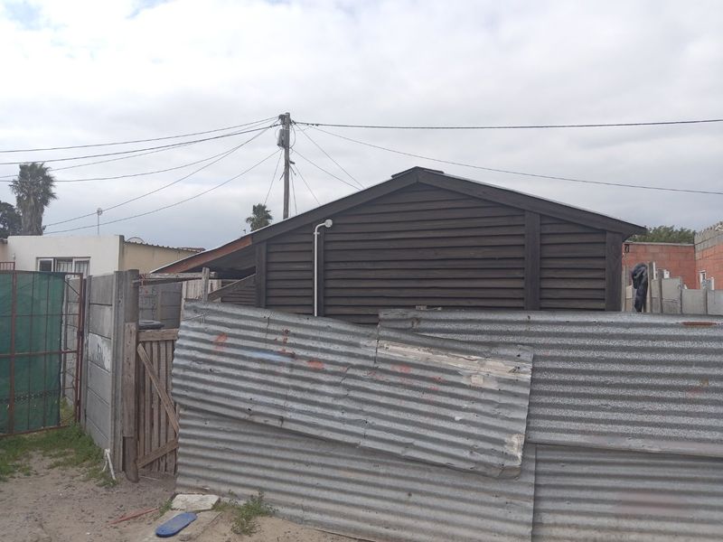 Rear view of the property featuring timber-clad structure, corrugated metal fencing, and precast concrete boundary walls.