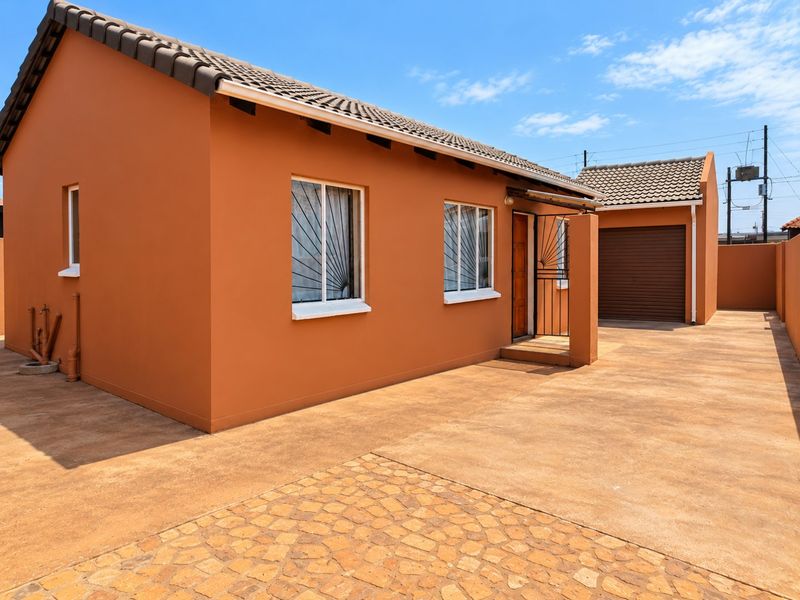 A well-maintained single-story house featuring a paved driveway, secure garage, and exterior security bars on the windows.
