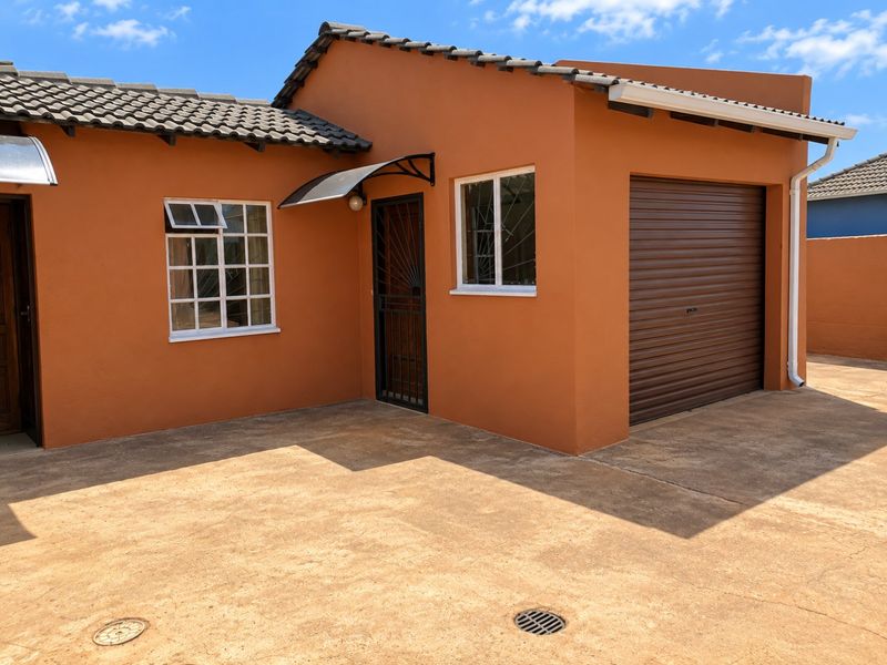 Front exterior view of the property featuring a roller garage door, security entrance gate, and a paved driveway area.