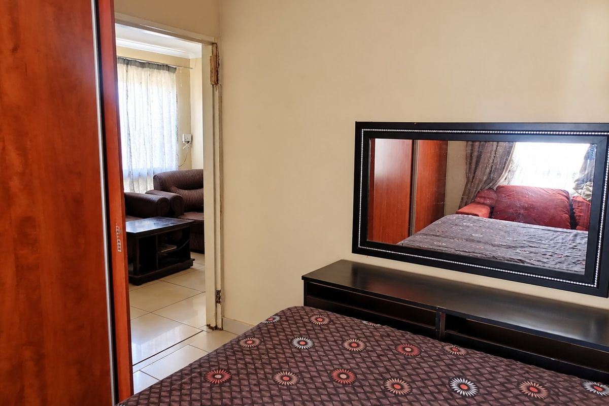 A bedroom featuring built-in wardrobe storage and tiled flooring, with an open doorway leading to an adjacent living area.