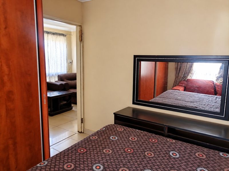 A bedroom featuring built-in wardrobe storage and tiled flooring, with an open doorway leading to an adjacent living area.