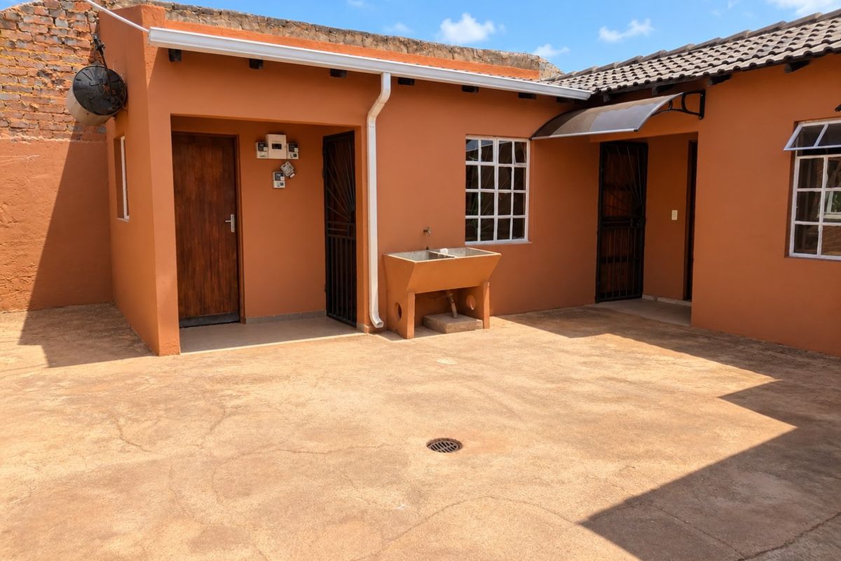 Rear courtyard area featuring a concrete wash trough, paved flooring with drainage, and access to multiple entry points with security gates.