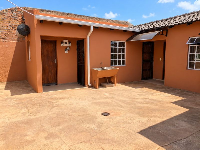 Rear courtyard area featuring a concrete wash trough, paved flooring with drainage, and access to multiple entry points with security gates.