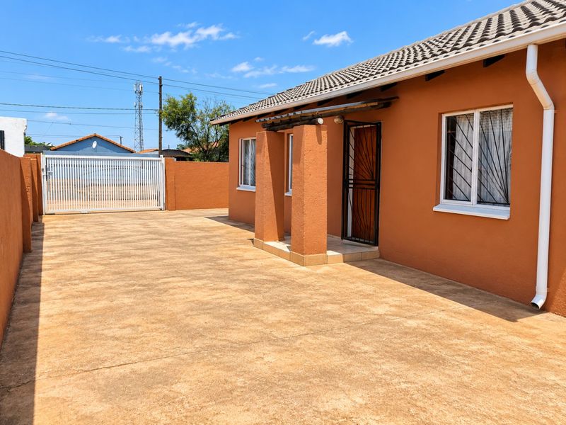 Front exterior view of the house featuring a paved driveway, secure entrance with security gate, and perimeter walling.