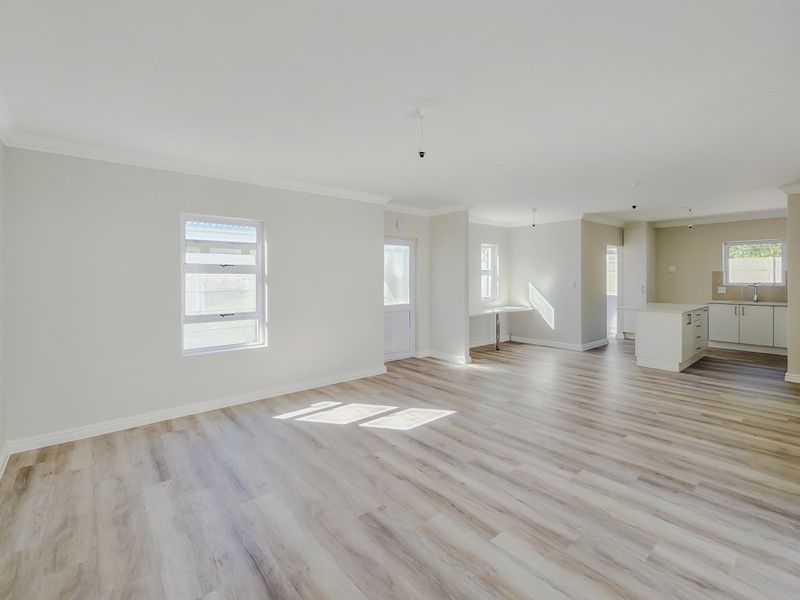 Spacious open-plan living area featuring modern laminate flooring, neutral walls, and a functional kitchen with built-in cabinetry and a central island.