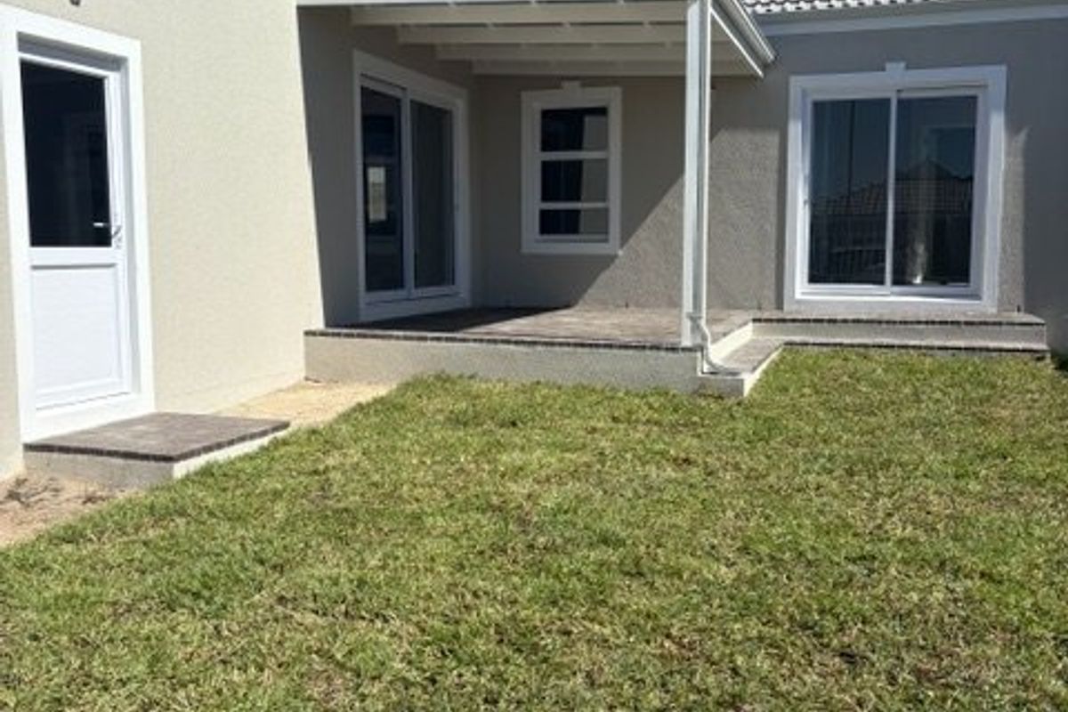 Rear view of the property featuring a covered patio area, sliding glass doors, and a well-maintained lawn.