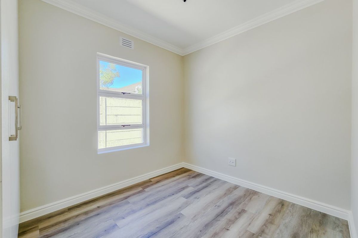 A bright, empty bedroom featuring modern laminate flooring, neutral walls, cornice detailing, and a built-in cupboard.