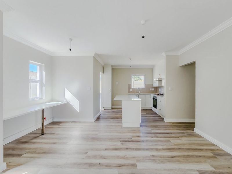 Bright open-plan living area featuring a modern kitchen with a central island, built-in appliances, and light wood-look laminate flooring throughout.