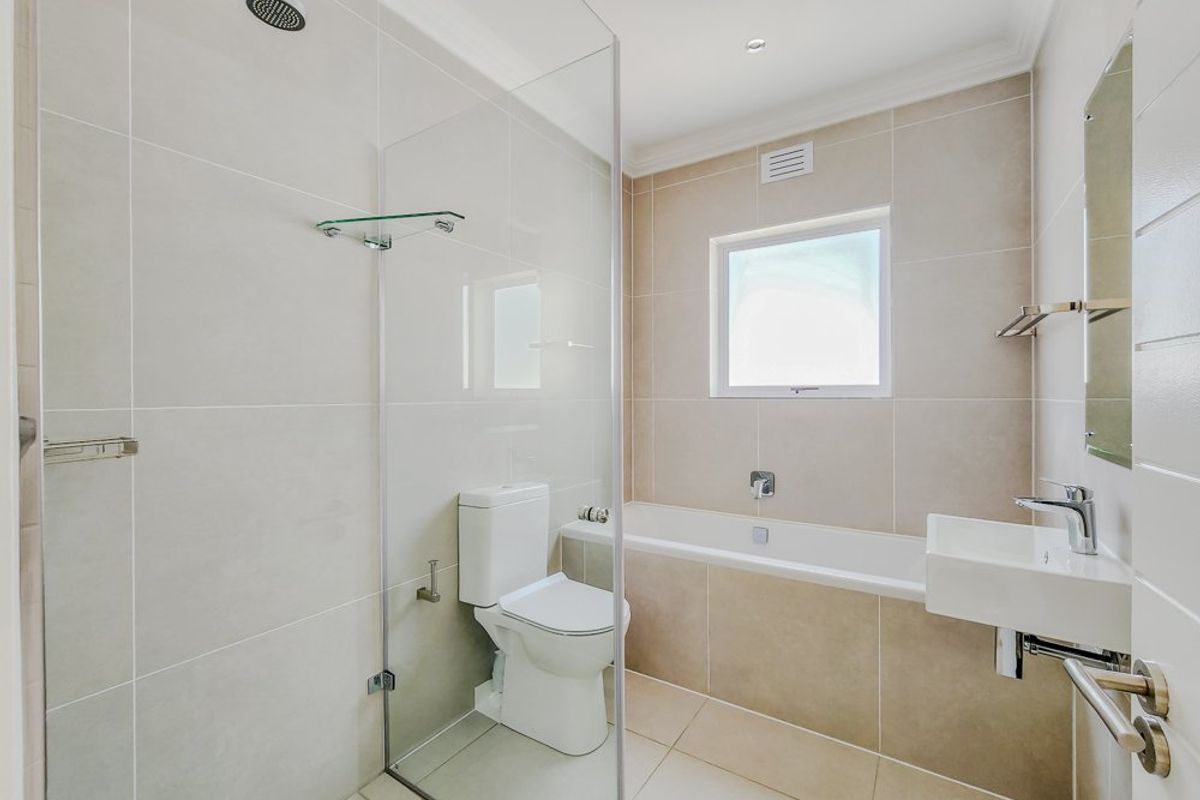 Modern, well-maintained bathroom featuring a walk-in shower with glass screen, built-in bathtub, wall-mounted basin, and neutral floor-to-ceiling tiling.