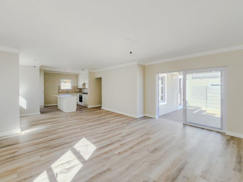 Spacious open-plan living area featuring modern laminate flooring, a sleek kitchen with island, and sliding glass doors leading to an outdoor patio.