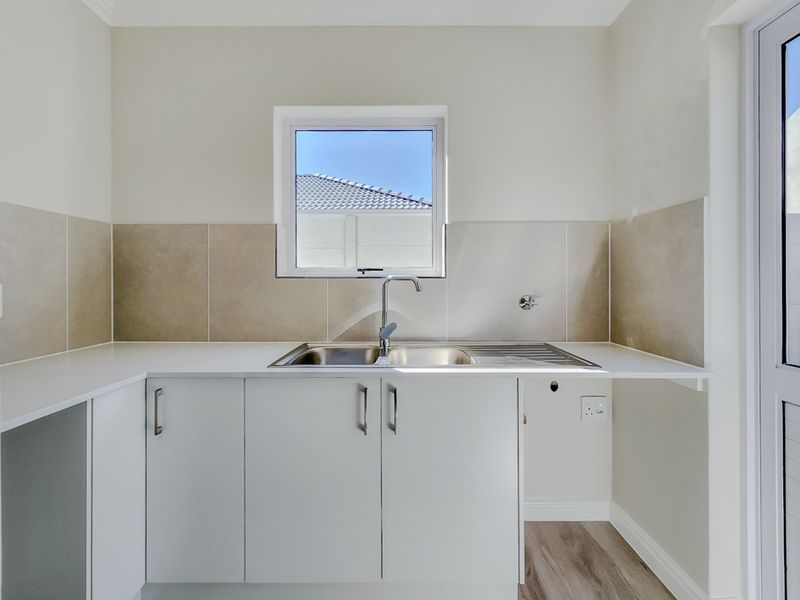 A clean and modern laundry area featuring built-in white cabinetry, a stainless steel sink, and neutral tiled splashbacks with direct outdoor access.