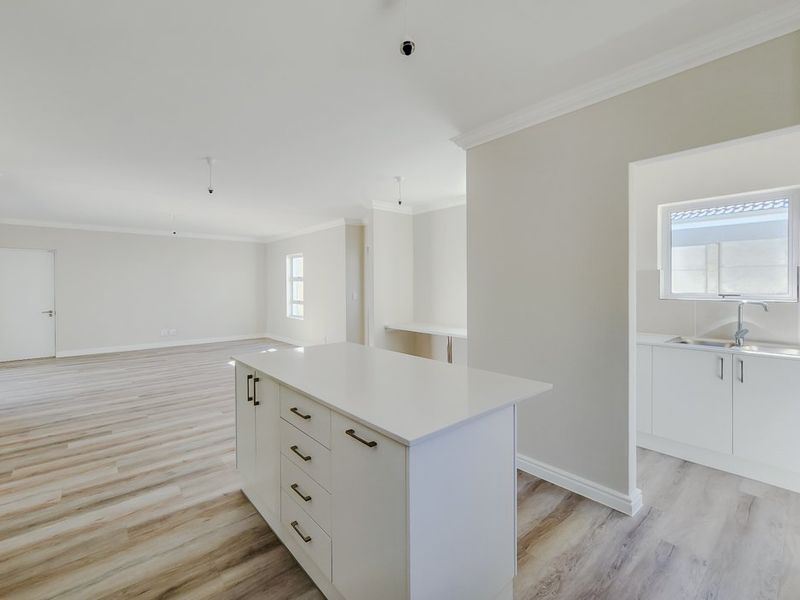 Spacious open-plan living area featuring a modern kitchen island, neutral finishes, and light wood-look laminate flooring throughout.