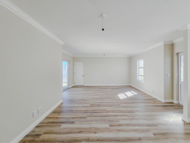 A bright, spacious, and empty living area featuring modern laminate flooring, crown molding, and access to an outdoor space through a sliding glass door.