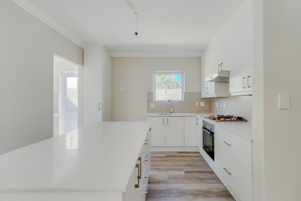 Modern, bright kitchen featuring a central island, sleek white cabinetry, built-in oven, hob, extractor fan, and durable laminate flooring.