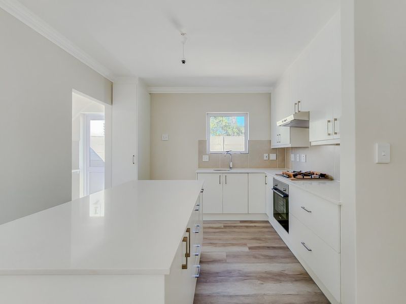 Modern, bright kitchen featuring a central island, sleek white cabinetry, built-in oven, hob, extractor fan, and durable laminate flooring.