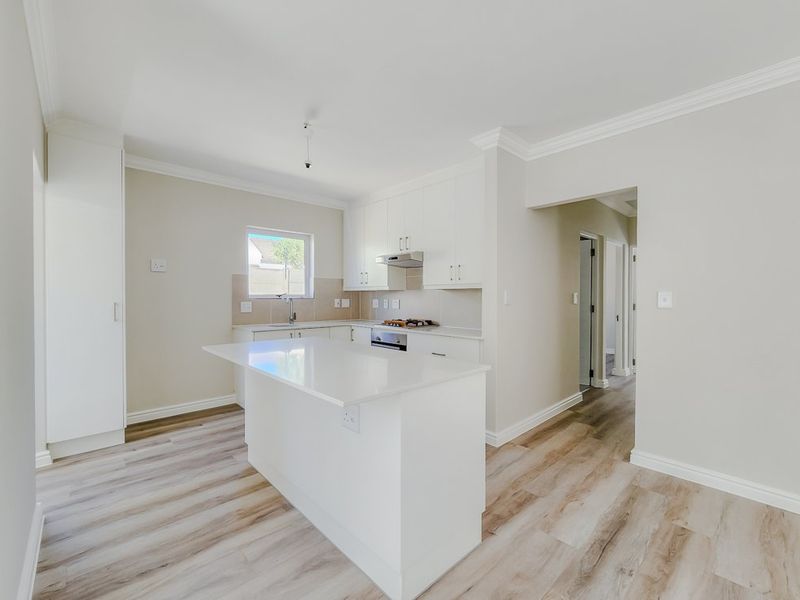 Modern, bright kitchen featuring white cabinetry, stone countertops, a central island, and integrated appliances, finished with light wood-look laminate flooring.
