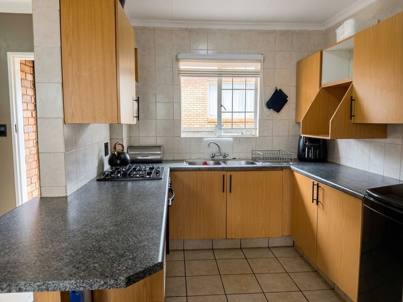 Functional kitchen featuring laminate cabinetry, granite-look countertops, a gas hob, and a double sink with tiled splashbacks.