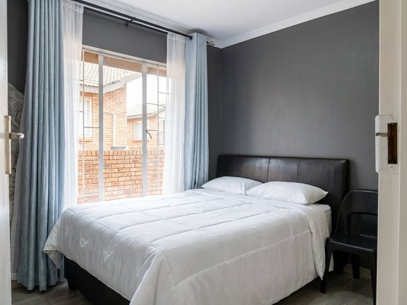 A well-maintained bedroom featuring dark grey walls, laminate flooring, and a large sliding window that allows for natural light.