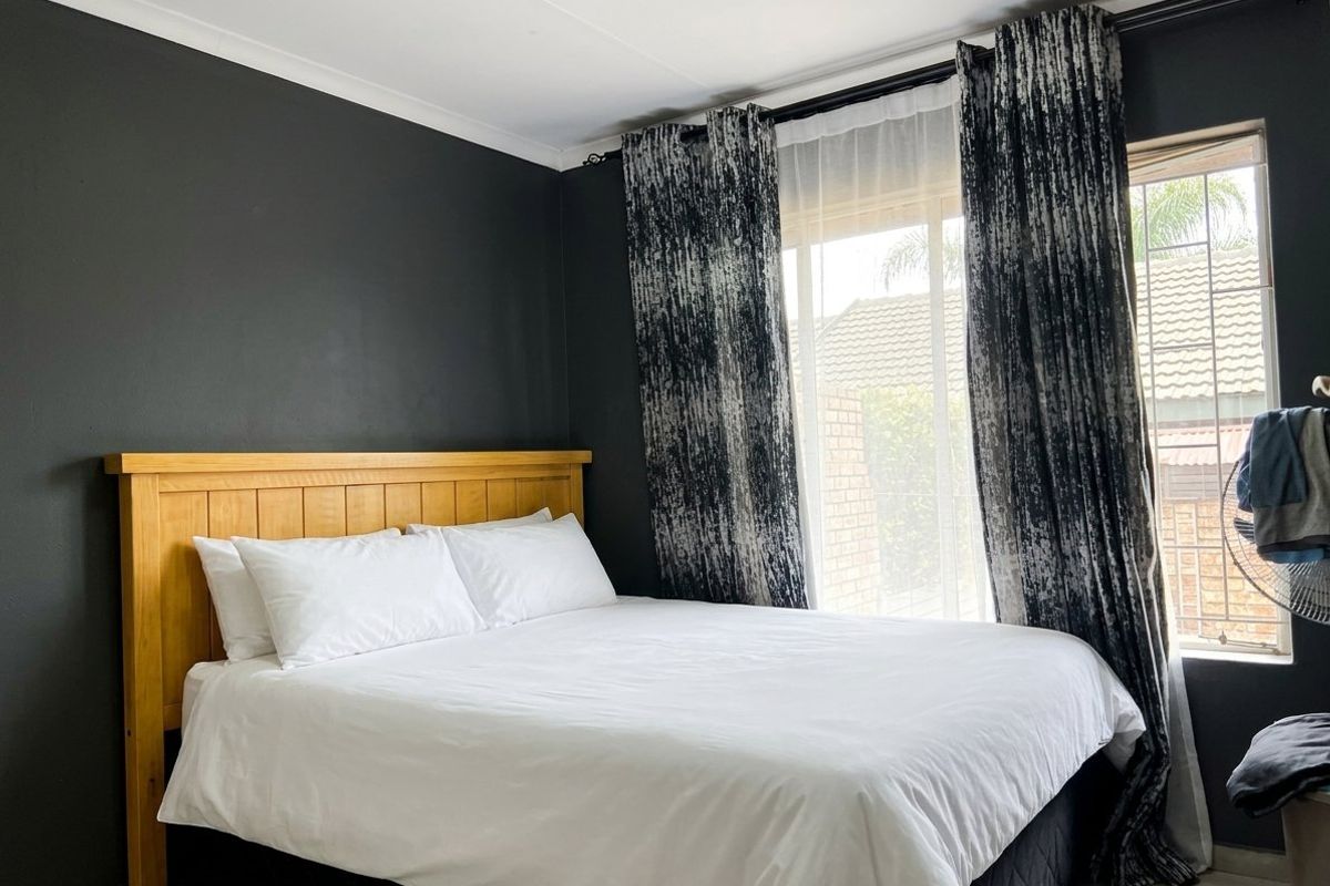 A well-maintained bedroom featuring dark accent walls, tiled flooring, and large windows with curtain rails, providing a comfortable and private living space.