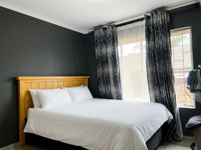 A well-maintained bedroom featuring dark accent walls, tiled flooring, and large windows with curtain rails, providing a comfortable and private living space.