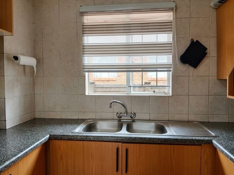 A functional kitchen area featuring a double bowl stainless steel sink, laminate countertops, and timber veneer cabinetry with tiled splashbacks.
