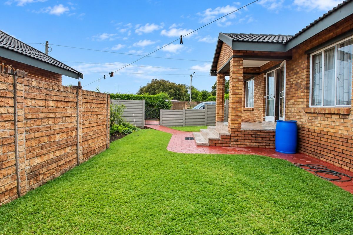 A well-maintained rear garden featuring a brick boundary wall, paved walkway, and a covered patio area attached to the main townhouse structure.