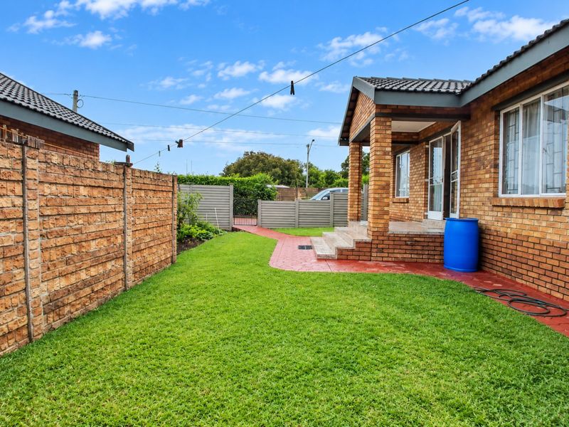 A well-maintained rear garden featuring a brick boundary wall, paved walkway, and a covered patio area attached to the main townhouse structure.