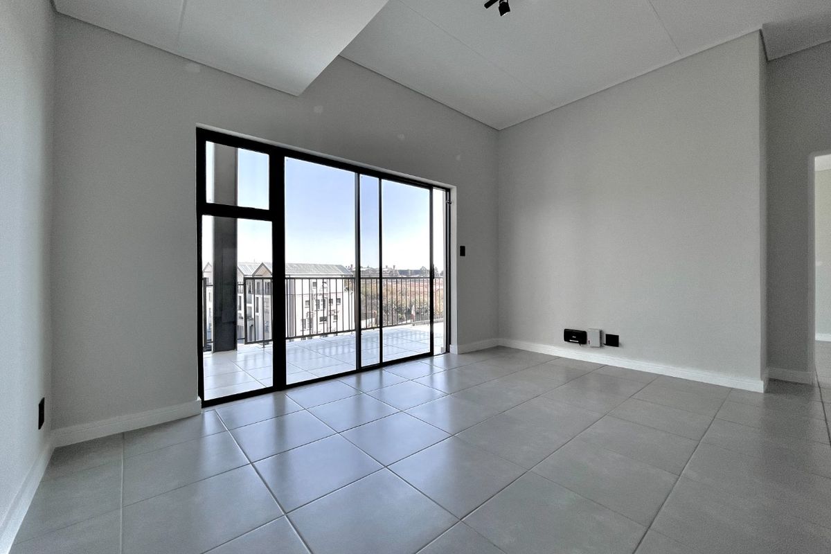 A bright, modern, and empty living room featuring large sliding glass doors leading to a balcony, neutral tiled floors, and contemporary track lighting.