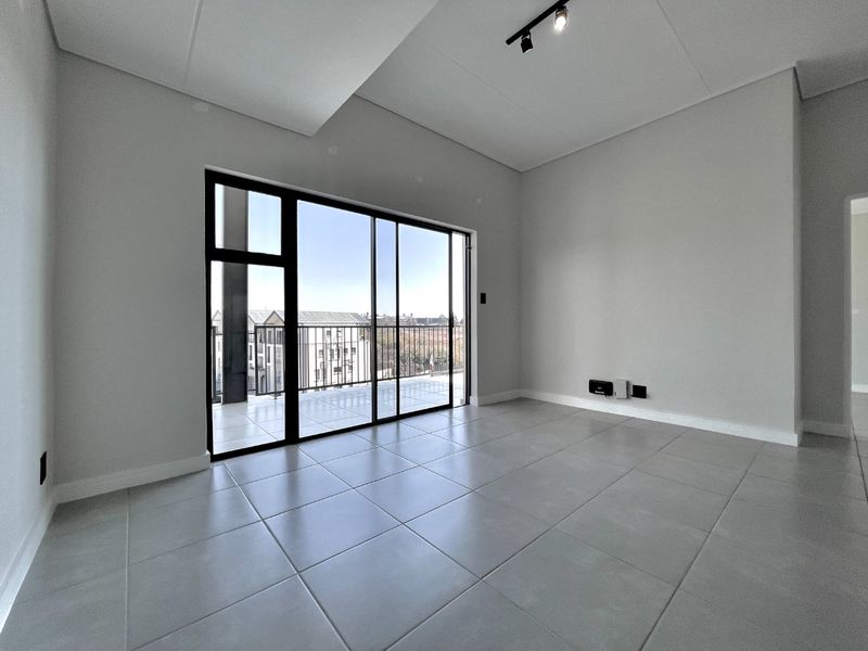 A bright, modern, and empty living room featuring large sliding glass doors leading to a balcony, neutral tiled floors, and contemporary track lighting.