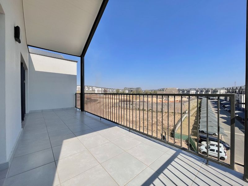 A spacious, covered balcony featuring clean tiled flooring and a secure metal balustrade, offering an open view of the surrounding neighborhood.