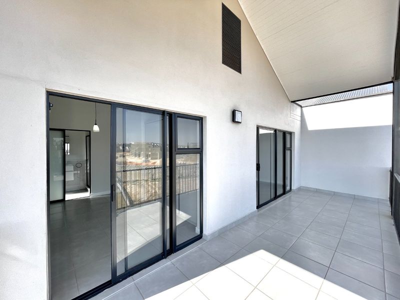 A spacious, modern covered balcony featuring tiled flooring, a high vaulted ceiling, and large sliding glass doors providing access to the interior.