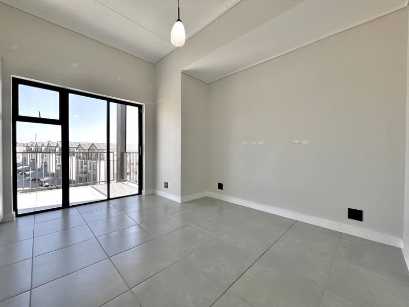 A bright, empty living area featuring large sliding glass doors leading to a balcony, neutral tiled flooring, and modern pendant lighting.